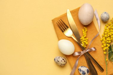 Table serving with Easter eggs and mimosa flowers on yellow background