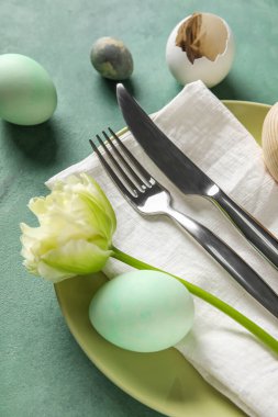 Table serving with Easter eggs and tulip flower on green grunge background, closeup
