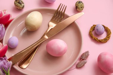 Table serving with Easter eggs on pink background, closeup