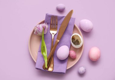 Table serving with Easter eggs and tulip flower on lilac background