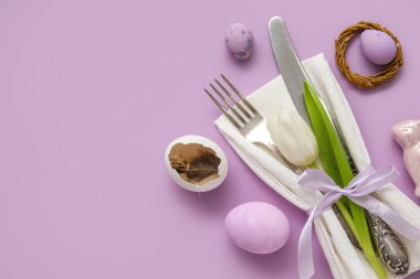 Table serving with Easter eggs and tulip flower on lilac background
