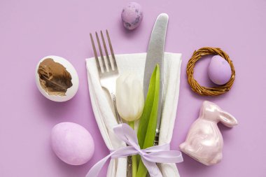 Table serving with Easter eggs, bunny and tulip flower on lilac background