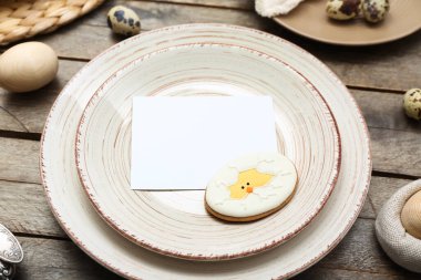Table setting with blank card and Easter cookie on wooden background