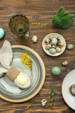 Table setting with Easter eggs, bunny and floral decor on brown wooden background
