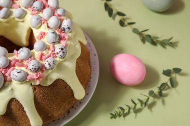 Plate with tasty Easter cake, eggs and eucalyptus branches on green background, closeup