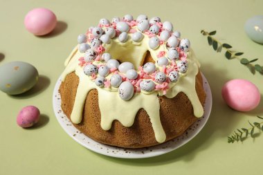 Plate with tasty Easter cake, eggs and eucalyptus branches on green background