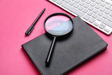 Notebook, pen, magnifier and keyboard on pink background, closeup. World Poetry Day celebration