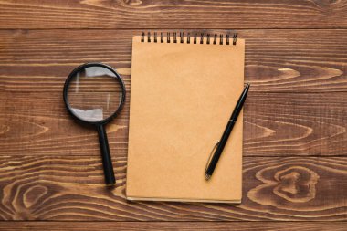 Blank notebook, magnifier and pen on wooden background. World Poetry Day celebration
