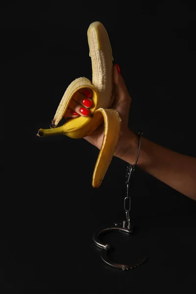 Woman with banana and handcuffs from sex shop on black background