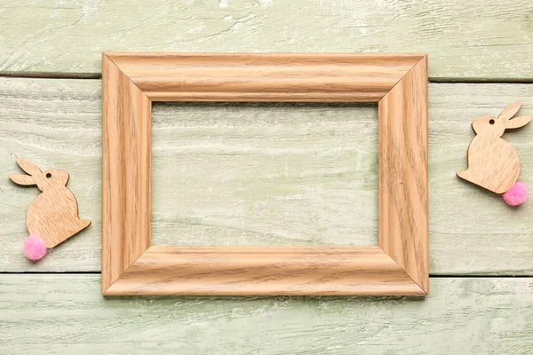 Blank frame and Easter bunnies on green wooden background