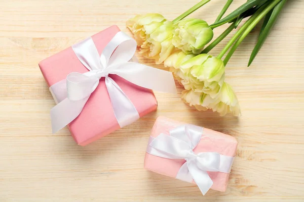 Gift boxes and beautiful tulip flowers on light wooden background. Hello spring