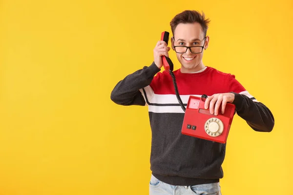 Happy young man with telephone on yellow background
