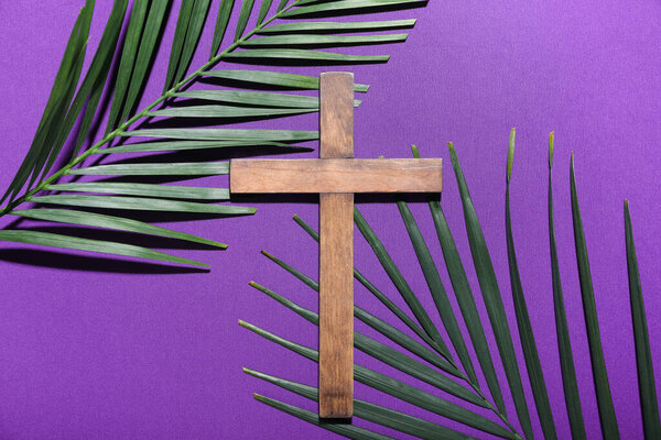 Wooden cross with palm leaves on purple background. Good Friday concept