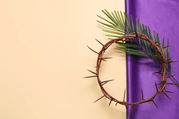 Crown of thorns with palm leaf and purple fabric on beige background. Good Friday concept