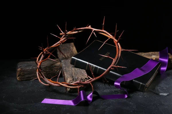 Crown of thorns with purple ribbon, Holy Bible and cross on dark background. Good Friday concept