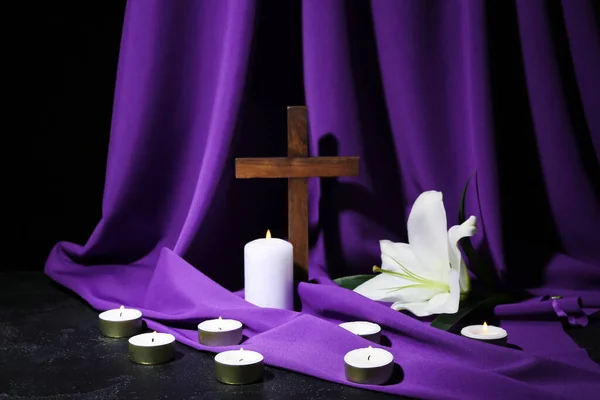 Cross with lily, burning candles and purple fabric on dark background. Good Friday concept