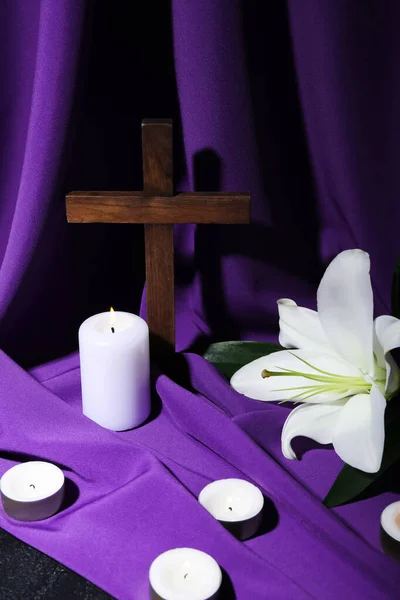 Cross with lily, burning candles on purple fabric. Good Friday concept