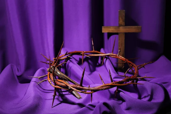 Crown of thorns with nails and cross on purple fabric. Good Friday concept