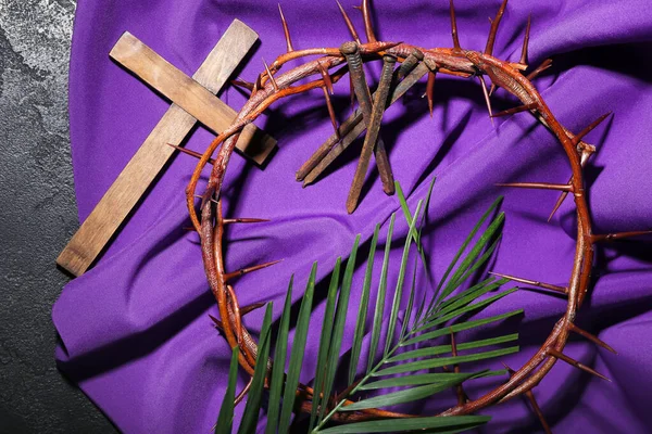 Crown of thorns with nails, cross, palm leaf and purple fabric on dark background. Good Friday concept