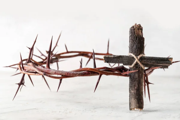 Wooden cross with crown of thorns on light background. Good Friday concept