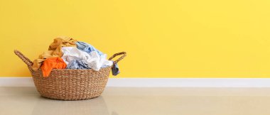Wicker basket with laundry near yellow wall. Banner for design