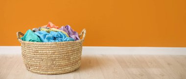 Wicker basket with laundry near orange wall. Banner for design
