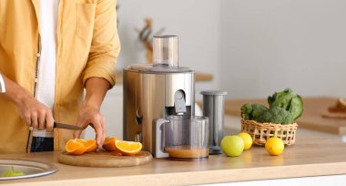 Young man with juicer preparing healthy fruit juice in kitchen