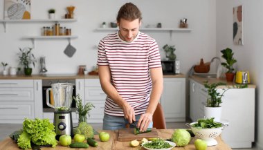 Young man with modern blender making green smoothie in kitchen at home