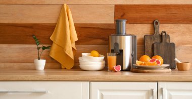 Modern juicer with fresh fruits and glass of beverage on table in kitchen