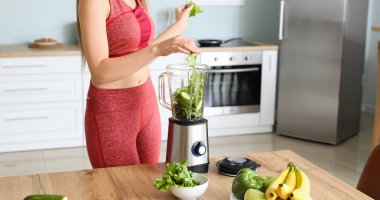 Sporty woman with modern blender making green smoothie in kitchen at home
