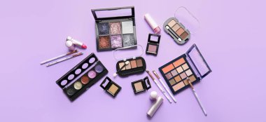 Set of makeup cosmetics with brushes on lilac background