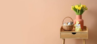 Basket with Easter eggs, rabbit and yellow tulips on wooden table near beige wall. Banner for design
