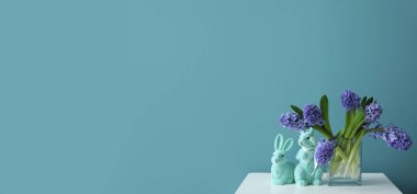 Vase with hyacinth flowers and Easter bunnies on table near blue wall. Banner for design