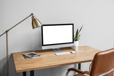 Modern table with computer, cup of coffee and houseplant near light wall