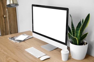 Modern table with computer, cup of coffee and houseplant near light wall