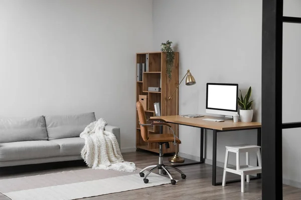 Interior of light office with table, modern computer and shelving unit