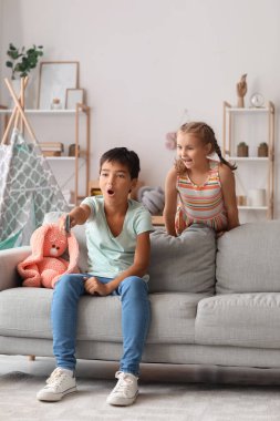 Surprised little boy and girl watching cartoons on TV at home