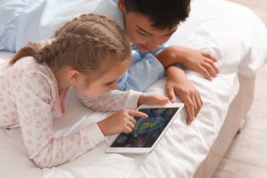 Little girl and her brother watching cartoons on tablet computer in bedroom, closeup
