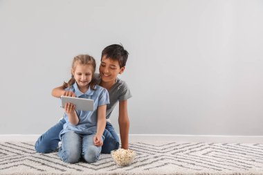 Little girl and her brother watching cartoons on tablet computer near light wall