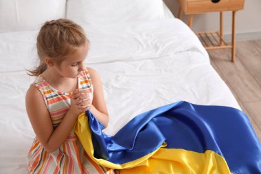 Little girl with flag of Ukraine praying in bedroom