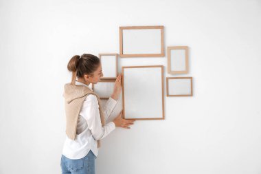 Young woman hanging blank frame on light wall at home