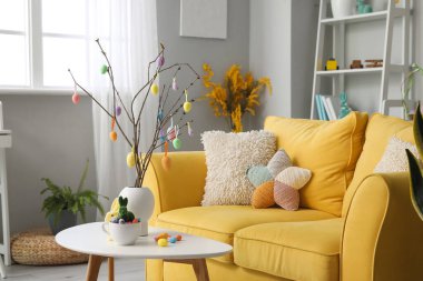 Vase with tree branches, Easter eggs, rabbits and cup on table in living room