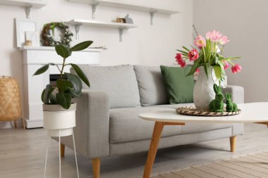 Vase with tulips and Easter rabbits on table in interior of living room