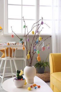 Vase with tree branches, Easter eggs, rabbits and cup on table in living room