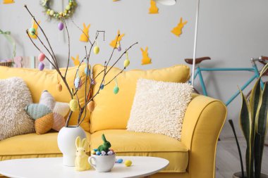 Vase with tree branches, Easter eggs, rabbits and cup on table in living room