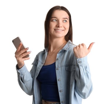 Young woman with mobile phone pointing at something on white background