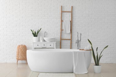 Interior of light bathroom with bathtub, sink and ladder