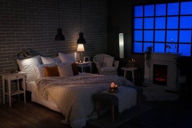 Interior of bedroom with cozy blankets on bed and burning candles at night