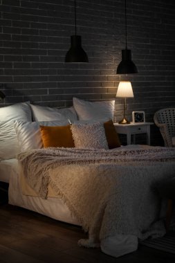 Interior of bedroom with cozy blankets on bed and burning candles at night