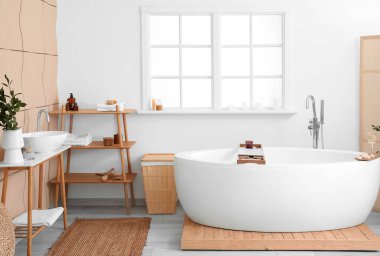 Interior of bathroom with modern bathtub, laptop, champagne and burning candles on board